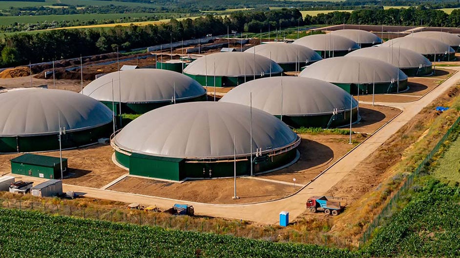 一個生物燃料設施，由兩排圓頂結構組成，坐落在一個農村設施的中間，周圍是田野和樹木。＂srcset=